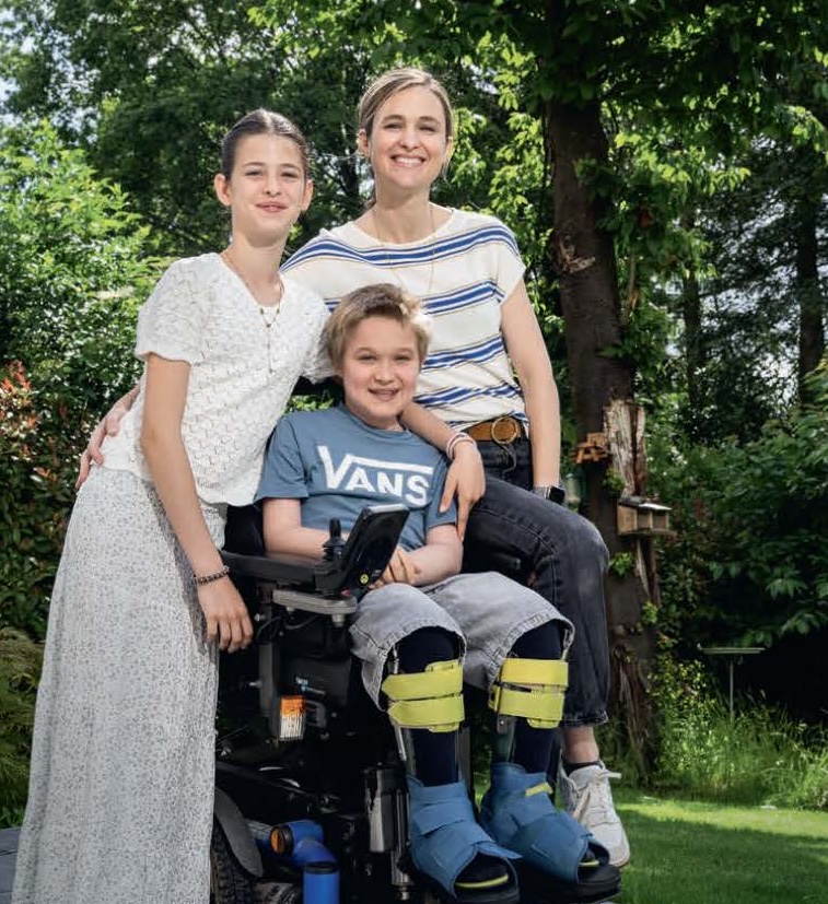 Oscar dans son fauteuil, entouré de sa maman Émilie et de sa sœur Ofélia, dans le jardin